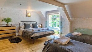 Een slaapkamer met een schuine plafond, een bed met hoofdeinde, een houten dressoir, een plant en een raam met uitzicht op groen.