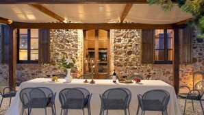 Un área de comedor al aire libre con un fondo de pared de piedra, vigas de madera y una mesa cubierta con sillas.