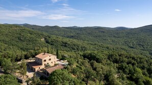 Un edificio de piedra con techo de tejas rodeado de un bosque denso y colinas.