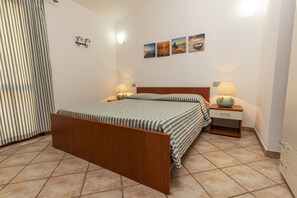 Une chambre à coucher avec un lit en bois, deux tables de chevet avec des lampes, un rideau à rayures et quatre tableaux accrochés au mur.