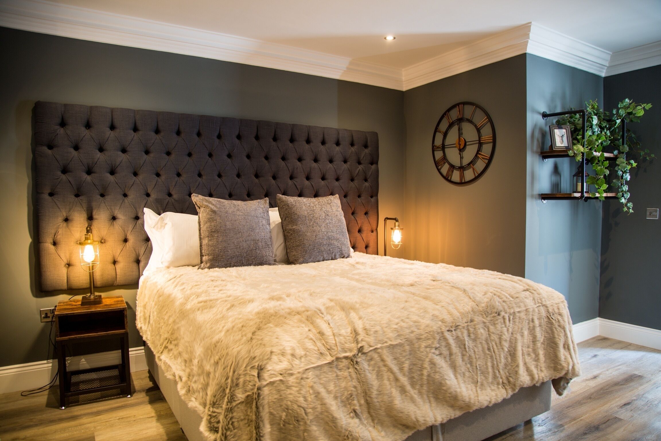 A bedroom with a tufted headboard, a large bed with a fluffy blanket, two bedside lamps, and a wall clock.