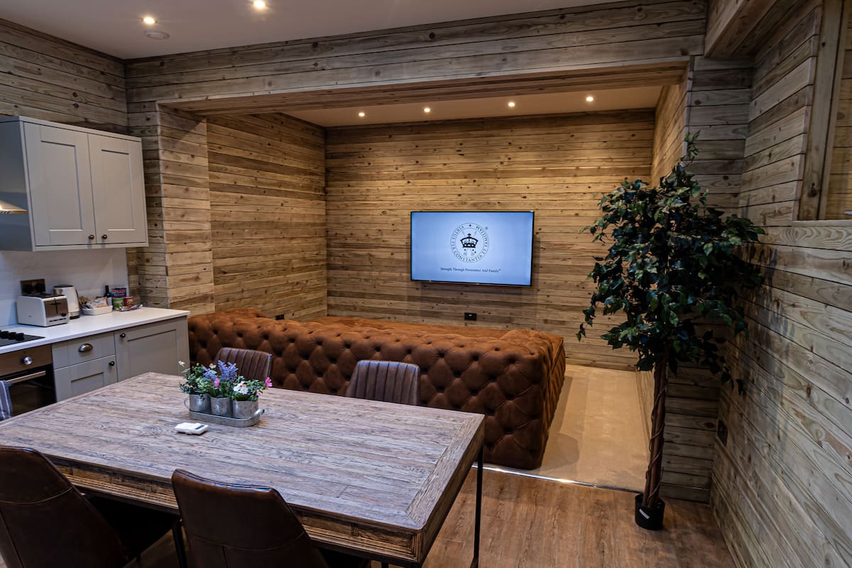 A modern kitchen with built-in appliances, a dining area with a wooden table and leather chairs, and a seating area with a tufted sofa.