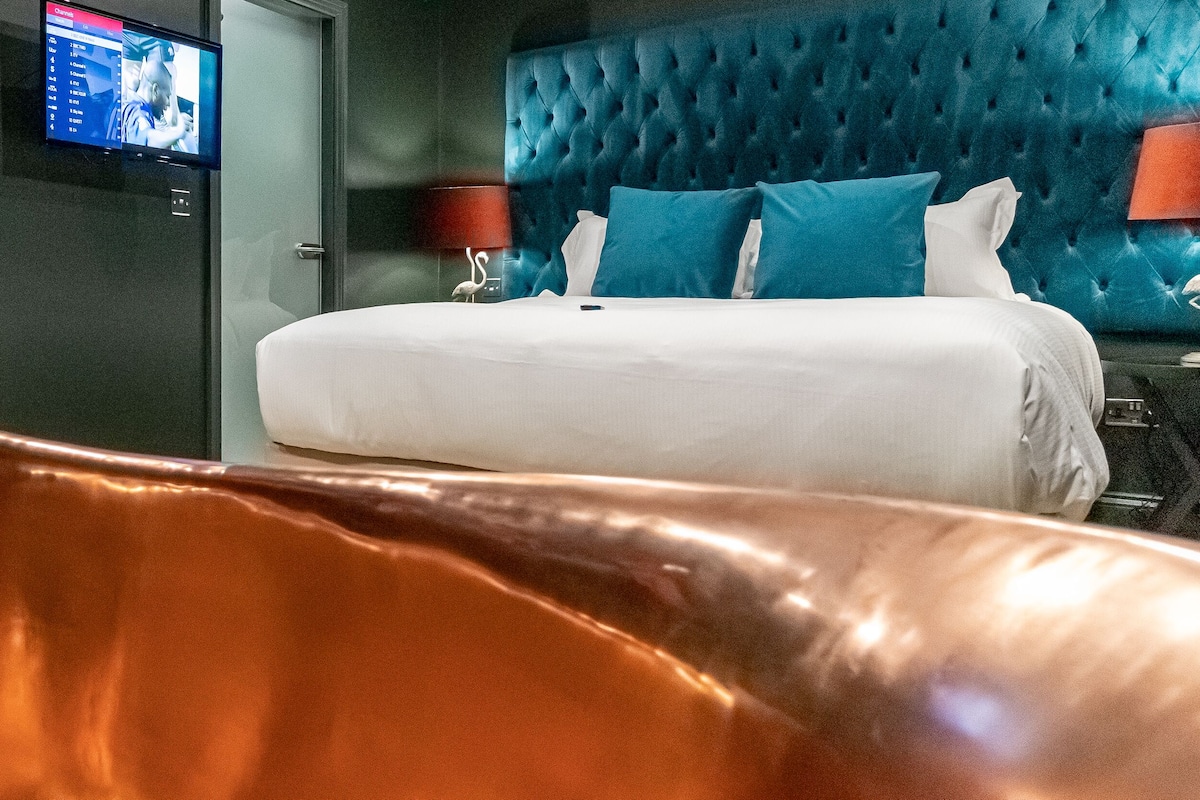 A hotel room with a tufted headboard, a bed with white bedding, two bedside tables with lamps, and a television on the wall.