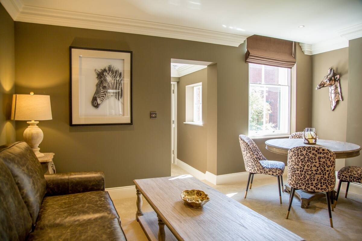 A living room with a sofa, a coffee table, a framed zebra artwork, a dining area with a round table and leopard print chairs, and a window with a view.