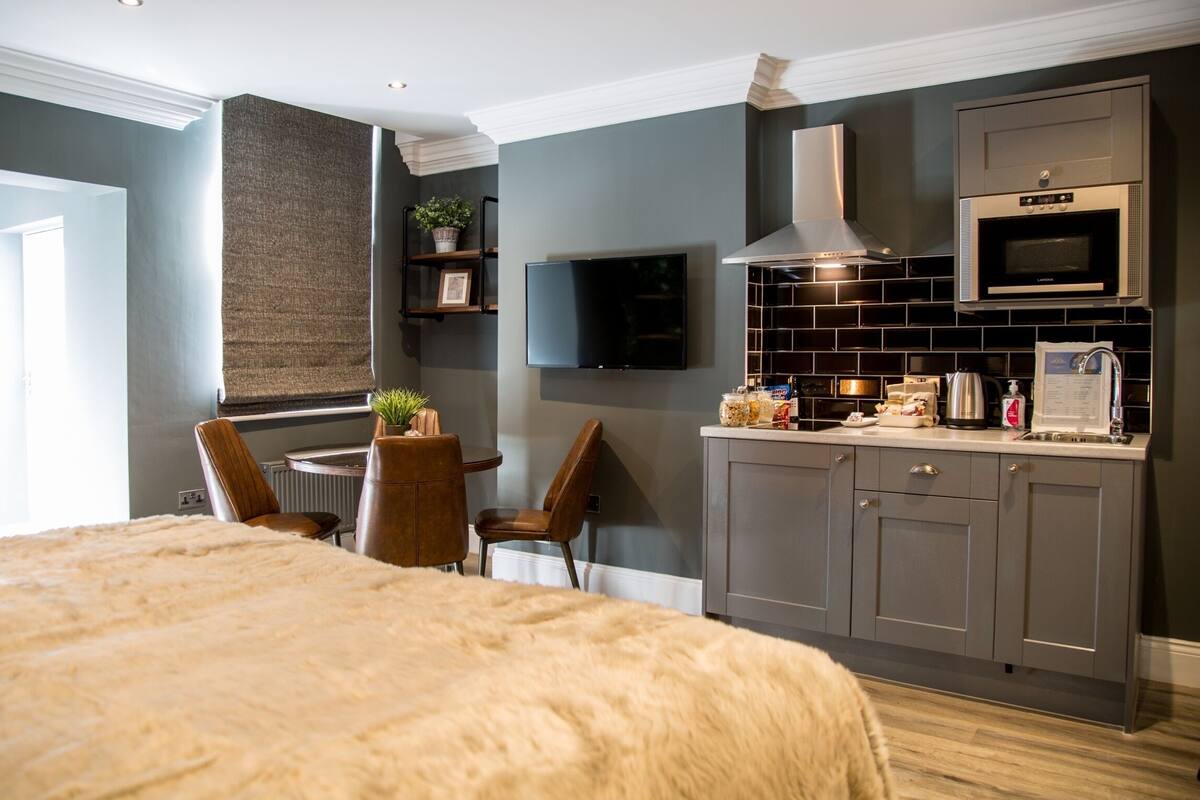 A modern kitchen with a flat-screen TV, stainless steel appliances, and a dining area with a sofa and chairs.
