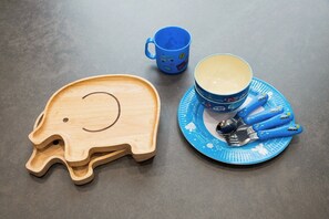A table with a wooden elephant-shaped tray, a blue mug, a blue plate with a spoon set, and a cup.