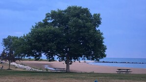 A beach with a large tree, picnic tables, and a grassy area. - Trendy! Pro Cleaned, Self Check In - Sleeps 10 (Pleasant Prairie)