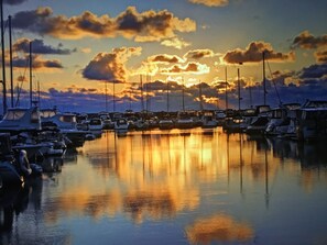 En småbåtshamn med förtöjda båtar, stilla vatten som speglar himlen och en solnedgång i bakgrunden.