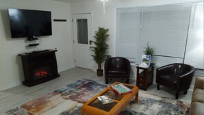 A living room with a flat-screen TV, a fireplace, a coffee table, two leather chairs, and a large window with blinds. - Trendy! Pro Cleaned, Self Check In - Sleeps 10 (Pleasant Prairie)