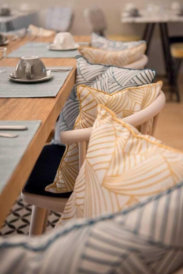 A dining area with a long table, chairs with patterned cushions, and a cup on the table. - T Boutique Hotel (Arcachon)