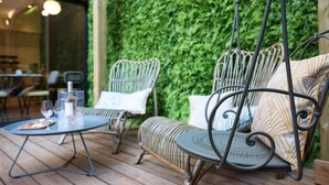 Ein Patio mit Korbmöbeln, einem Tisch, einem Hängesessel und einer grünen Wand.