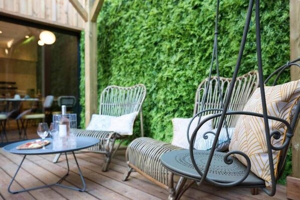 A patio area with wicker chairs and a table, a hanging chair, and a green wall. - T Boutique Hotel (Arcachon)