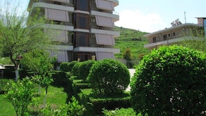 A multi-story building with balconies, surrounded by well-maintained greenery and a hilly landscape. - Denta Hotel (Orikum)