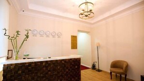 A reception area with a wooden reception desk, a chandelier, clocks on the wall, and a chair. - Hermes Hotel (Tirana)
