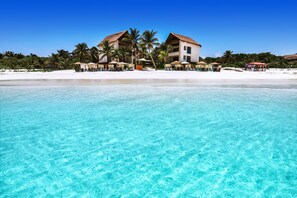 Ein Strandhotel mit klarem türkisblauem Wasser, Palmen und Strandstühlen.