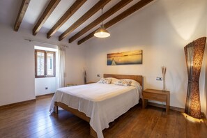 Ein Schlafzimmer mit einem hölzernen Bett, einem Nachttisch, einem Beistelltisch, einem Bild an der Wand und einem Fenster mit Vorhängen.