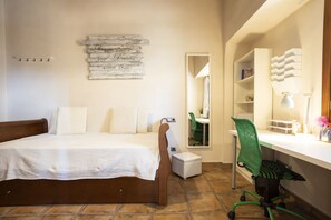 A bedroom with a bed, a desk, a chair, a mirror, and a wall-mounted shelf.