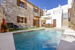 A swimming pool with lounge chairs and a stone building with wooden shutters.