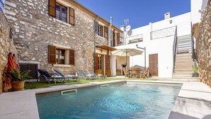 Una piscina amb gandules i un edifici de pedra amb persianes de fusta.