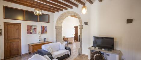 Una sala de estar acogedora con sofá, televisor y un arco de piedra que conduce a otra habitación.