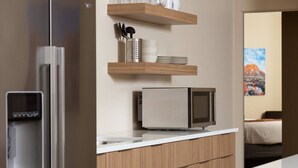 Une cuisine moderne dotée d’un four à micro-ondes encastré, d’un distributeur d’eau et d’étagères en bois au-dessus du plan de travail.