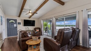 A spacious living room with a brown leather sofa, a wicker coffee table, and a ceiling fan. - Lakefront w/ Dock, 300mb WIFI, Theater, Arcade (Tool)
