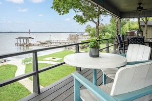 Une terrasse avec une table et des chaises donnant sur une étendue d’eau, une pelouse et un quai agrémenté d’un belvédère.