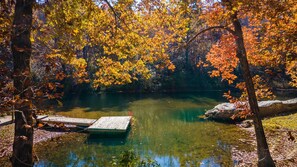 Un lac paisible, bordé d’un feuillage automnal, avec une jetée en bois et un ciel dégagé.