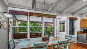 Uma sala de jantar com mesa de madeira, cadeiras verdes e vista para o exterior através de grandes janelas.