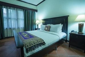 Habitación de hotel con una cama grande, dos lámparas de noche, una mesita de noche con un teléfono y una ventana con cortinas.