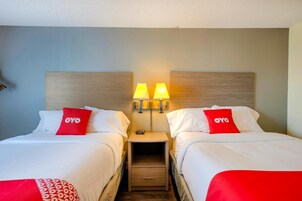 Habitación de hotel con dos camas, cada una con un almohadón rojo, una mesita de noche con lámpara y un cabecero de madera.