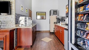 A compact kitchen with a stone backsplash, wooden cabinets, a refrigerator, a microwave, and a beverage dispenser. - Oyo Hotel Downtown Castle Rock (Castle Rock)