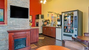 A restaurant with a stone wall, wooden cabinets, a TV, a vending machine, and a dining area with a table and chairs. - Oyo Hotel Downtown Castle Rock (Castle Rock)