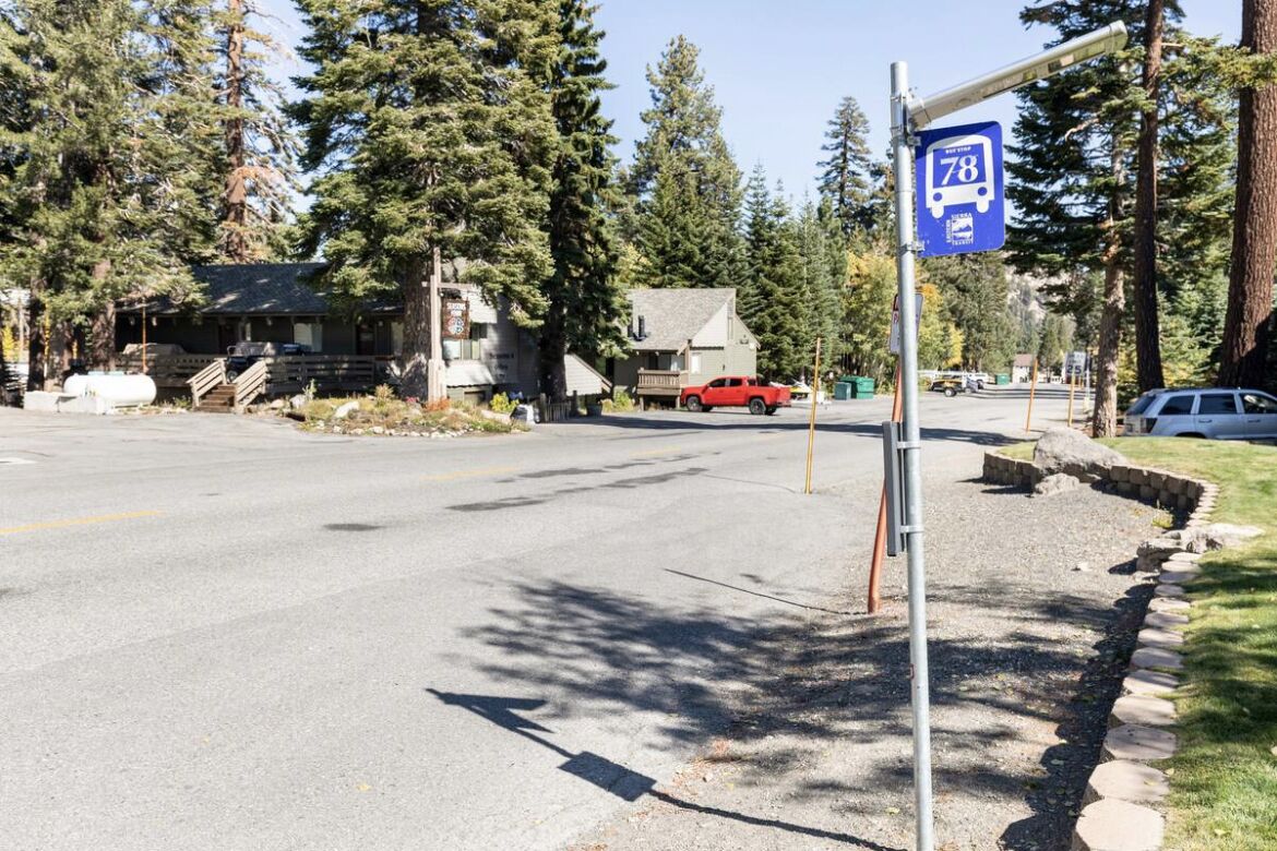 A road with a bus stop sign, a red vehicle, and a building with a porch.