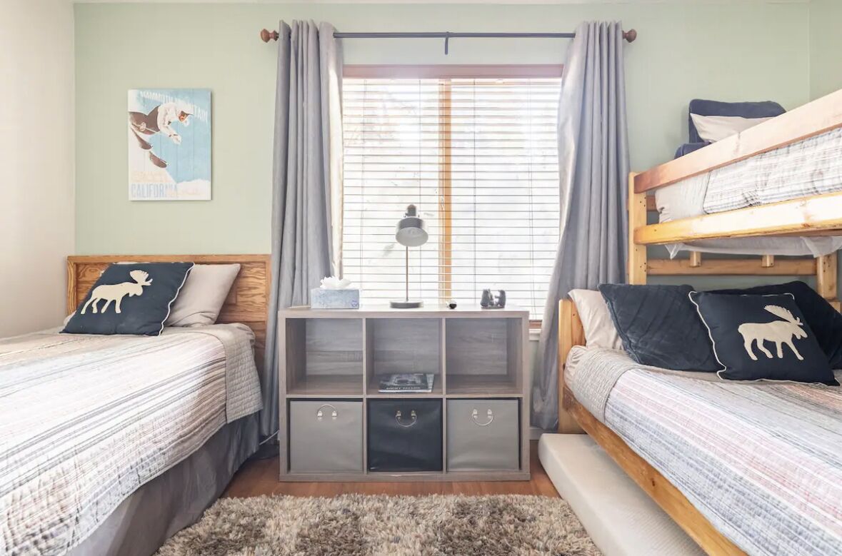 A bedroom with two bunk beds, a wooden desk with storage, a window with curtains, and a wall-mounted lamp.
