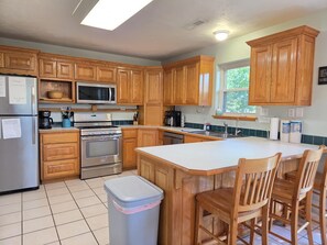 A kitchen with wooden cabinets, a stainless steel refrigerator, a microwave, a stove, and a sink.
