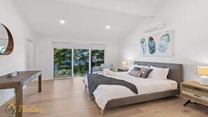 A modern bedroom with a large bed, a desk, and a view of greenery through the sliding doors. - Randall Drive No 64 - Magnificent Views - Pool - Air con - WiFi - The list goes on! (Salamander Bay)