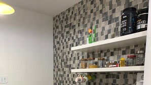 Eine moderne Küche mit schwarzer Arbeitsplatte, weißen Schränken und einer gemusterten Spritzschutzwand. Auf der Arbeitsfläche befinden sich verschiedene Küchengeräte und Utensilien.