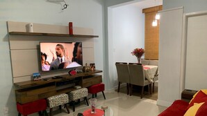 Ein Wohnzimmer mit Flachbildfernseher, einer Holz-Unterhaltungsecke, einer Essecke mit Tisch und Stühlen sowie einem roten Sofa.