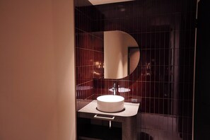 Un baño moderno con un lavabo redondo, un espejo y un perchero para toallas.
