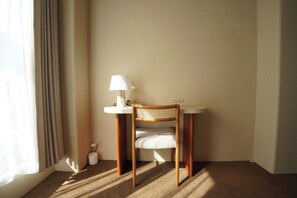 Una habitación de esquina con una silla de madera, una mesa blanca con una lámpara y un pequeño bote de basura blanco.