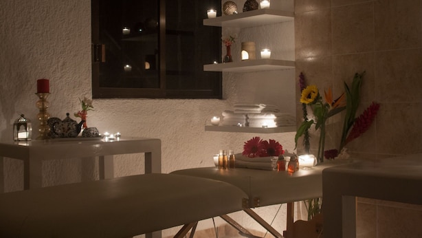 A dimly lit room with a white wall, a window, and shelves with candles and flowers. - Hotel Boutique Xoxula (San Pedro Cholula)
