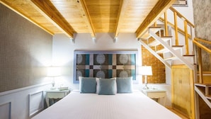 A bedroom with a large bed, wooden ceiling beams, a checkered wall art piece, and a staircase. - Hotel Boutique Xoxula (San Pedro Cholula)
