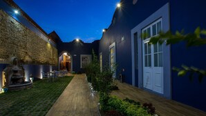 A courtyard with a wooden pathway, a fountain, and a seating area with chairs. There are doors and windows on the building, and the area is well-lit. - Hotel Boutique Xoxula (San Pedro Cholula)