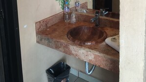 A bathroom with a stone sink, a mirror, and a wall-mounted light fixture. - Casa Calli Hotel Restaurante Spa (San Pedro Cholula)