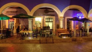 An outdoor dining area with tables and chairs, umbrellas, and a building with arches in the background. - Casa Calli Hotel Restaurante Spa (San Pedro Cholula)