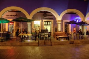 An outdoor dining area with tables and chairs, umbrellas, and a building with arches in the background. - Casa Calli Hotel Restaurante Spa (San Pedro Cholula)