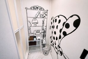 A hallway with a white wall featuring a black and white line drawing of a room with a bookshelf, a lamp, and a mirror.