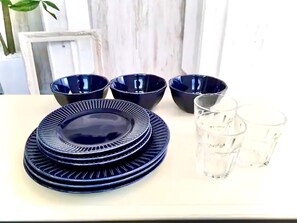 Ett bord med staplade blå tallrikar och skålar, två glas vatten och en krukväxt i bakgrunden.