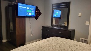 Un dormitorio con cama, cómoda, televisor montado en la pared y espejo sobre la cómoda.